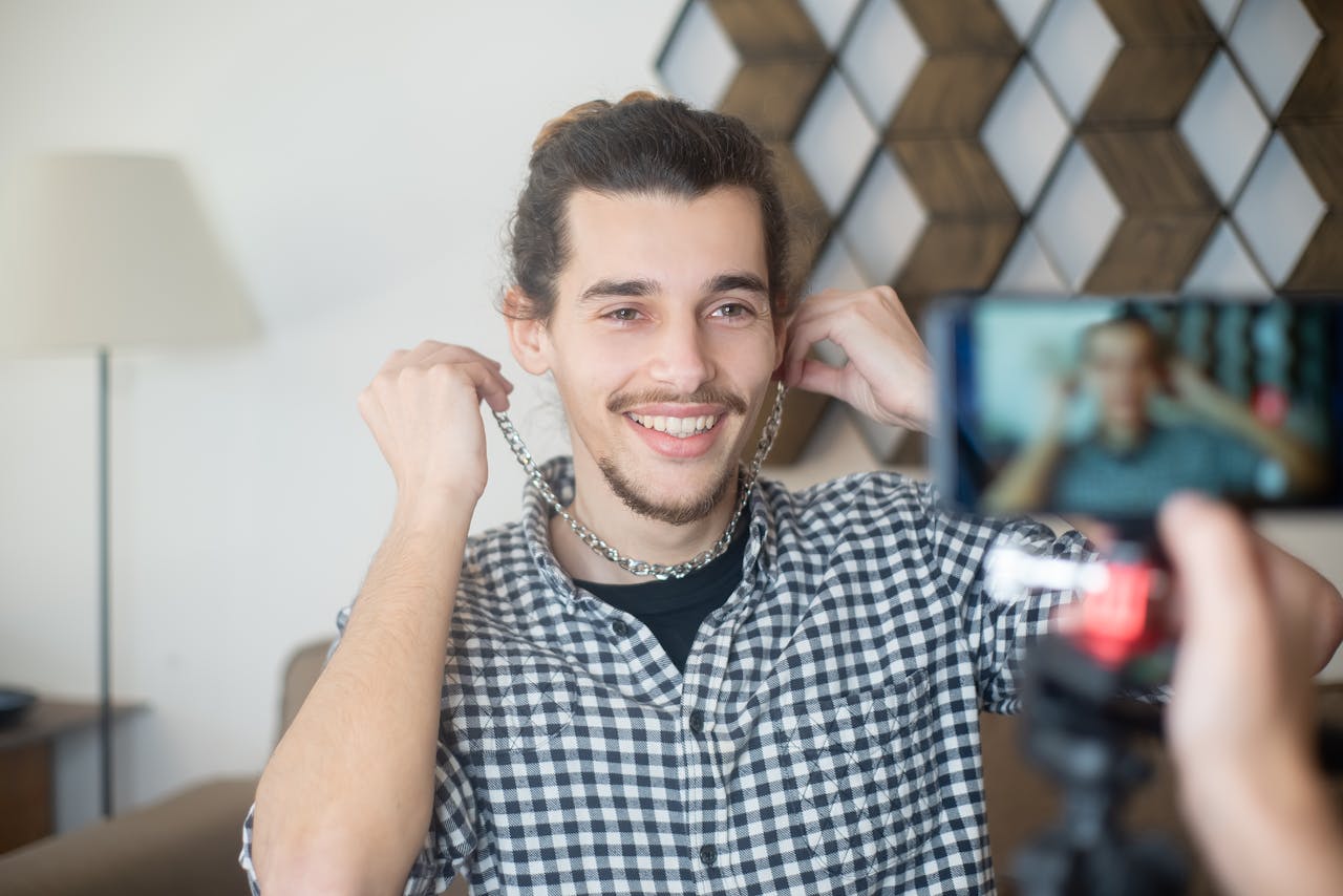 embark Smiling man vlogging indoors with a smartphone camera, creating online content.